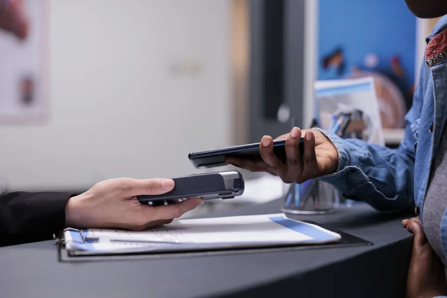 Customer making a contactless payment by tapping a smartphone against a handheld card terminal at a reception counter